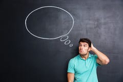 Jeune homme confus réfléchi se tenant et pensant au-dessus du fond de tableau noir images stock Jeune homme confus réfléchi se tenant et pensant au-dessus du fond de tableau noir images stock