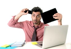 Jeune homme d'affaires occupé au bureau fonctionnant avec le comprimé numérique de téléphone portable et l'ordinateur portable d' photographie stock Jeune homme d'affaires occupé au bureau fonctionnant avec le comprimé numérique de téléphone portable et l'ordinateur portable d' photographie stock