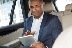 Jeune homme d'affaires s'asseyant sur le siège arrière dans la voiture jouant le jeu sur le comprimé numérique joyeux photo stock Jeune homme d'affaires s'asseyant sur le siège arrière dans la voiture jouant le jeu sur le comprimé numérique joyeux photo stock