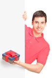 Jeune homme retenant un cadeau et une position derrière le panneau Photos stock Jeune homme retenant un cadeau et une position derrière le panneau Photos stock