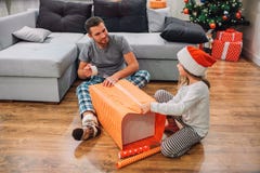 Jeune homme s'asseyant sur le plancher avec sa fille et presemt de emballage Il tient la bande dans les mains et les regards à el images libres de droits Jeune homme s'asseyant sur le plancher avec sa fille et presemt de emballage Il tient la bande dans les mains et les regards à el images libres de droits