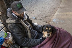 Jeune homme sans abri et son chien se trouvant sur le trottoir dans le sac de couchage images libres de droits Jeune homme sans abri et son chien se trouvant sur le trottoir dans le sac de couchage images libres de droits