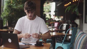 Jeune homme utilisant des écouteurs avec des fils à énumérer la musique en café, lieu de travail moderne se reposant en café Ordi clips vidéos Jeune homme utilisant des écouteurs avec des fils à énumérer la musique en café, lieu de travail moderne se reposant en café Ordi clips vidéos