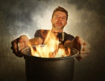 Jeune homme à la maison malpropre attirant et choqué de cuisinier avec le tablier tenant faire cuire le pot en feu brûlant la nou photos stock Jeune homme à la maison malpropre attirant et choqué de cuisinier avec le tablier tenant faire cuire le pot en feu brûlant la nou photos stock