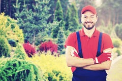Jeune jardinier de sourire avec les bras croisés se tenant dans le jardin photographie stock libre de droits Jeune jardinier de sourire avec les bras croisés se tenant dans le jardin photographie stock libre de droits