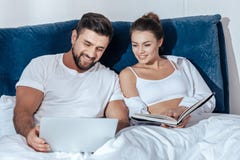Jeune lecture affectueuse de couples dans le lit image stock Jeune lecture affectueuse de couples dans le lit image stock