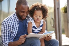 Jeune livre de lecture noir de père et de fille dehors photo libre de droits Jeune livre de lecture noir de père et de fille dehors photo libre de droits