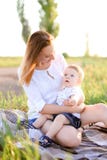 Jeune mère caucasienne s'asseyant avec peu d'enfant sur le plaid, herbe sur le fond images stock Jeune mère caucasienne s'asseyant avec peu d'enfant sur le plaid, herbe sur le fond images stock
