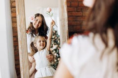 Jeune mère et son petit support avec du charme de fille devant le miroir dans la chambre avec l'arbre de nouvelle année photo stock Jeune mère et son petit support avec du charme de fille devant le miroir dans la chambre avec l'arbre de nouvelle année photo stock