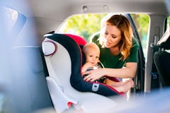 Jeune mère mettant le bébé garçon dans le siège de voiture Image libre de droits Jeune mère mettant le bébé garçon dans le siège de voiture Image libre de droits