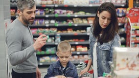 Jeune mère, père et enfant et choix des bonbons dans le magasin de nourriture, prise des produits et puis les regarder de famille clips vidéos Jeune mère, père et enfant et choix des bonbons dans le magasin de nourriture, prise des produits et puis les regarder de famille clips vidéos