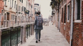 Jeune touriste européen élégant heureux de femme avec la caméra appréciant la marche le long de la vieille rue célèbre de canal à clips vidéos Jeune touriste européen élégant heureux de femme avec la caméra appréciant la marche le long de la vieille rue célèbre de canal à clips vidéos
