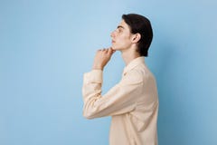 Jeune type aux cheveux foncés mince beau avec des yeux bleus utilisant la main jaune de participation de chemise sur le menton po images stock Jeune type aux cheveux foncés mince beau avec des yeux bleus utilisant la main jaune de participation de chemise sur le menton po images stock