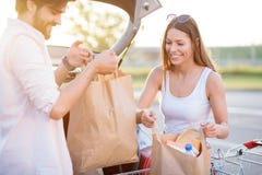 Jeunes couples de sourire déchargeant des sacs d'épicerie de caddie image stock Jeunes couples de sourire déchargeant des sacs d'épicerie de caddie image stock