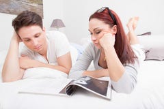 Jeunes couples en magazine de lecture de lit ensemble photo stock Jeunes couples en magazine de lecture de lit ensemble photo stock