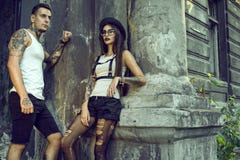 Jeunes couples tatoués élégants dans des shorts noirs se tenant à la colonne de la vieille maison ruinée photographie stock libre de droits Jeunes couples tatoués élégants dans des shorts noirs se tenant à la colonne de la vieille maison ruinée photographie stock libre de droits