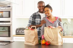 Jeunes couples éclatant des achats dans la cuisine moderne photographie stock libre de droits Jeunes couples éclatant des achats dans la cuisine moderne photographie stock libre de droits
