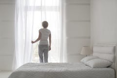 Jeunes jolis rideaux en ouverture de fille pendant le matin pour obtenir l'air frais, vue arrière photos libres de droits Jeunes jolis rideaux en ouverture de fille pendant le matin pour obtenir l'air frais, vue arrière photos libres de droits