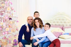 Jeunes parents heureux s'asseyant avec des fils près de l'arbre de sapin sur le lit photos libres de droits Jeunes parents heureux s'asseyant avec des fils près de l'arbre de sapin sur le lit photos libres de droits