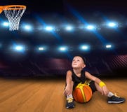 Jogador de basquetebol do menino com uma bola que senta-se no assoalho no gym e em sonhos de grandes vitórias imagem de stock royalty free Jogador de basquetebol do menino com uma bola que senta-se no assoalho no gym e em sonhos de grandes vitórias imagem de stock royalty free