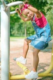 Jolie petite fille dans le costume de denim et jeux rouges de bandana sur le terrain de jeu des enfants images stock Jolie petite fille dans le costume de denim et jeux rouges de bandana sur le terrain de jeu des enfants images stock