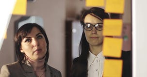 Jong meisje en Midden oude bedrijfsvrouw die de ontwerper van de glasmuur met post-itnota's bekijken en ideeën op hen verbinden stock videobeelden Jong meisje en Midden oude bedrijfsvrouw die de ontwerper van de glasmuur met post-itnota's bekijken en ideeën op hen verbinden stock videobeelden