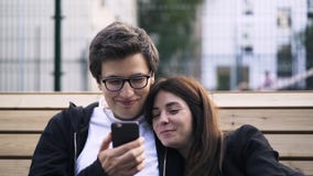 Jong paar die op een video op een smartphone buiten letten stock footage Jong paar die op een video op een smartphone buiten letten stock footage