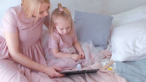 Jonge aantrekkelijke blonde vrouw met haar weinig charmante dochter die in roze kleding op iets in tabletzitting letten stock video Jonge aantrekkelijke blonde vrouw met haar weinig charmante dochter die in roze kleding op iets in tabletzitting letten stock video