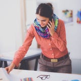 Jonge aantrekkelijke vrouwelijke manierontwerper die bij bureau werkt, dat terwijl het spreken op mobiel trekt Stock Afbeelding Jonge aantrekkelijke vrouwelijke manierontwerper die bij bureau werkt, dat terwijl het spreken op mobiel trekt Stock Afbeelding
