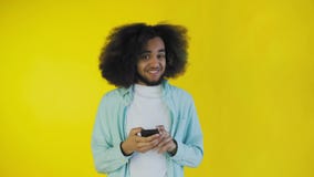 Jonge Afro-Amerikaanse mens gebruikend telefoon en krijgend goed nieuws op gele achtergrond Concept emoties stock videobeelden Jonge Afro-Amerikaanse mens gebruikend telefoon en krijgend goed nieuws op gele achtergrond Concept emoties stock videobeelden