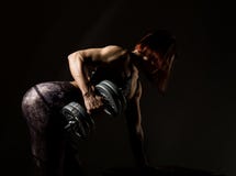Jonge atletische vrouw in sportkleding met een dumbbellson een donkere achtergrond stock afbeeldingen Jonge atletische vrouw in sportkleding met een dumbbellson een donkere achtergrond stock afbeeldingen