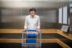 Jonge Aziatische mens die zich met karretjekar bevinden in lift of elevatior royalty-vrije stock afbeeldingen Jonge Aziatische mens die zich met karretjekar bevinden in lift of elevatior royalty-vrije stock afbeeldingen