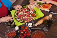 Jonge geitjes die een pizza maken die - de ingrediënten plaatsen op doug royalty-vrije stock afbeeldingen Jonge geitjes die een pizza maken die - de ingrediënten plaatsen op doug royalty-vrije stock afbeeldingen