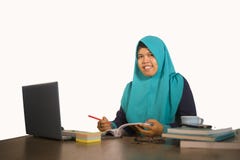 Jonge gelukkige en succesvolle Moslimstudentenvrouw in traditionele Islam hijab hoofdsjaal die aan bureau werken die met laptop b stock foto Jonge gelukkige en succesvolle Moslimstudentenvrouw in traditionele Islam hijab hoofdsjaal die aan bureau werken die met laptop b stock foto
