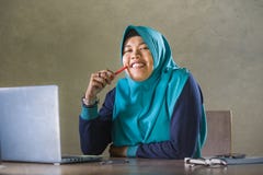 Jonge gelukkige en succesvolle Moslimstudentenvrouw in traditionele Islam hijab hoofdsjaal die aan bureau werken die met laptop b stock afbeeldingen Jonge gelukkige en succesvolle Moslimstudentenvrouw in traditionele Islam hijab hoofdsjaal die aan bureau werken die met laptop b stock afbeeldingen
