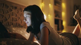 Jonge glimlachende vrouw die tabletcomputer voor het delen van sociale media met behulp van die in bed thuis bij nacht liggen Stock Fotografie Jonge glimlachende vrouw die tabletcomputer voor het delen van sociale media met behulp van die in bed thuis bij nacht liggen Stock Fotografie