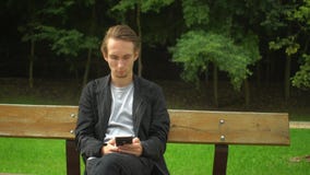 Jonge het gebruikssmartphone van de hipstermens voor sociale netwerken en heeft een rust in een park stock videobeelden Jonge het gebruikssmartphone van de hipstermens voor sociale netwerken en heeft een rust in een park stock videobeelden