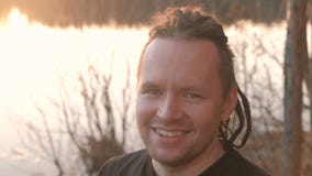 Jonge mens die met dreadlocks de camera en het glimlachen bekijken Tribunes op riverbank Het gezicht van de close-up stock footage Jonge mens die met dreadlocks de camera en het glimlachen bekijken Tribunes op riverbank Het gezicht van de close-up stock footage
