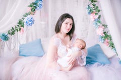 Jonge moeder in een boudoirkleding met een baby in haar wapens door het luifelbed stock fotografie Jonge moeder in een boudoirkleding met een baby in haar wapens door het luifelbed stock fotografie
