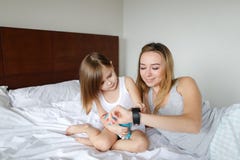 Jonge mooie moeder gebruikend slimme wathc en liggend op bed met weinig dochter Royalty-vrije Stock Afbeeldingen Jonge mooie moeder gebruikend slimme wathc en liggend op bed met weinig dochter Royalty-vrije Stock Afbeeldingen