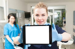 Jonge tandarts die moderne tablet met terug medewerker in haar gebruiken stock afbeelding Jonge tandarts die moderne tablet met terug medewerker in haar gebruiken stock afbeelding