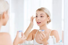 Jonge vrouw die op contactlenzen bij badkamers zetten stock foto's Jonge vrouw die op contactlenzen bij badkamers zetten stock foto's