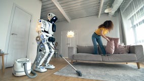 Jonge vrouwenspelen met hoofdkussens terwijl de witte robot het schoonmaken zuigt stock videobeelden Jonge vrouwenspelen met hoofdkussens terwijl de witte robot het schoonmaken zuigt stock videobeelden