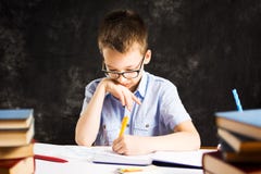 Jongen die in notitieboekje op het bureau schrijven dat in boeken wordt geregeld stock afbeelding Jongen die in notitieboekje op het bureau schrijven dat in boeken wordt geregeld stock afbeelding