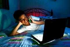 Jovem adolescente na frente de um laptop e em uma cama e em usar um telefone celular ou um smartphone Imagens de Stock Royalty Free Jovem adolescente na frente de um laptop e em uma cama e em usar um telefone celular ou um smartphone Imagens de Stock Royalty Free