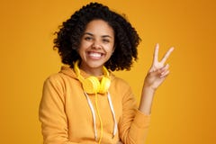 Jovem mulher afro-americano atrativa com sorriso brilhante vestida na roupa ocasional e nos fones de ouvido que mostram o gesto d imagem de stock Jovem mulher afro-americano atrativa com sorriso brilhante vestida na roupa ocasional e nos fones de ouvido que mostram o gesto d imagem de stock