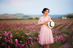 A jovem mulher bonita com o chapéu de palha que olha o por do sol nas rosas coloca Aroma, cosméticos e propaganda do perfume imagens de stock A jovem mulher bonita com o chapéu de palha que olha o por do sol nas rosas coloca Aroma, cosméticos e propaganda do perfume imagens de stock