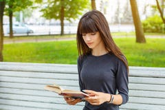 Jovem mulher bonita que senta-se em um banco na rua que lê um livro imagem de stock Jovem mulher bonita que senta-se em um banco na rua que lê um livro imagem de stock