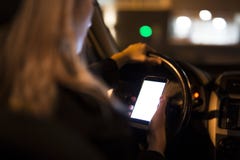 Jovem mulher bonita que usa seu telefone esperto ao conduzir seu carro na noite foto de stock Jovem mulher bonita que usa seu telefone esperto ao conduzir seu carro na noite foto de stock