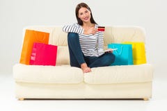 Jovem mulher com assento de compra do cartão de crédito no sofá com sacos de papel e roupa nova Fotografia de Stock Royalty Free Jovem mulher com assento de compra do cartão de crédito no sofá com sacos de papel e roupa nova Fotografia de Stock Royalty Free